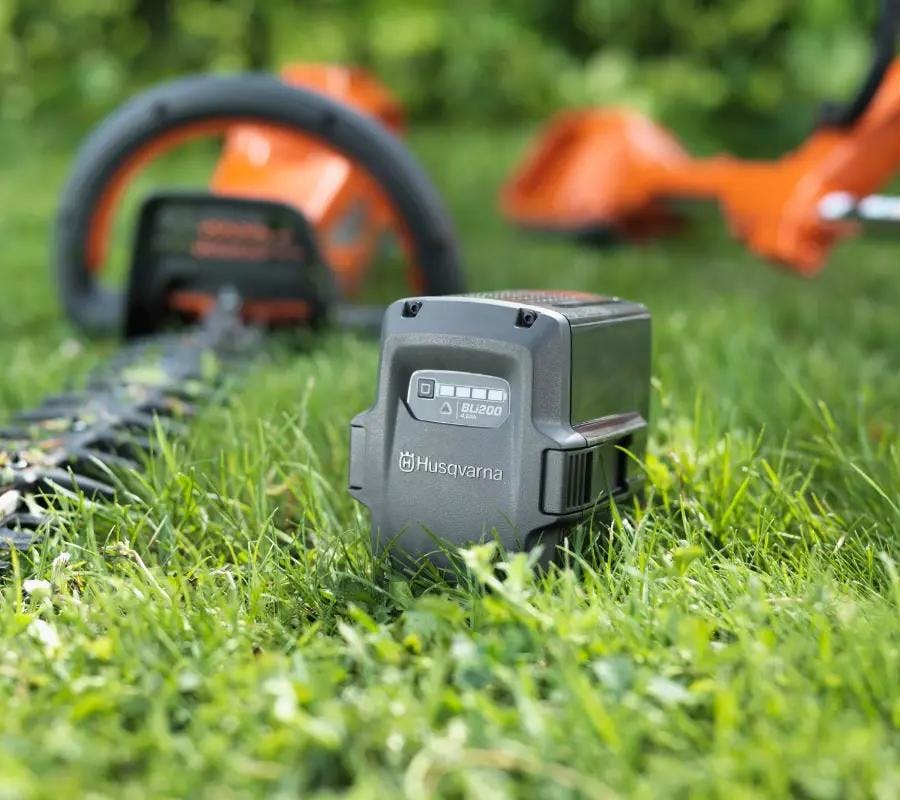 husqvarna battery sitting in grass with tools sitting behind